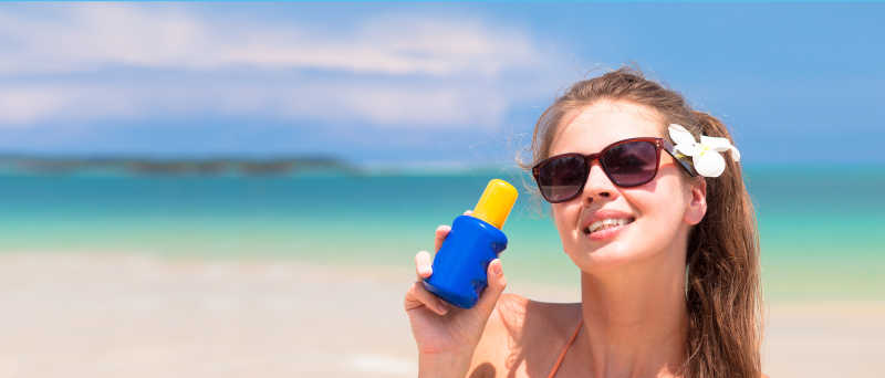海滩上拿着防晒霜戴墨镜的美女