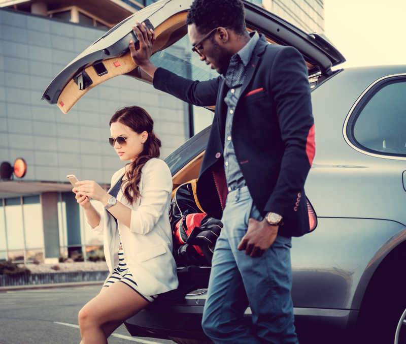 国际商人夫妇拿着智能手机站在汽车旁边