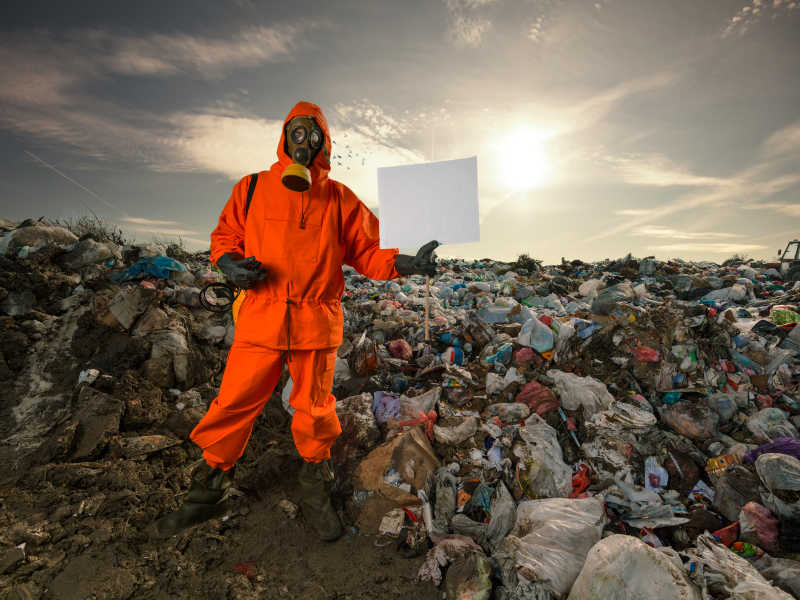 拿着空白纸板站在垃圾填埋场的回收工作者