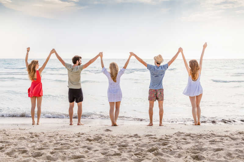 一群朋友举着双手面向大海