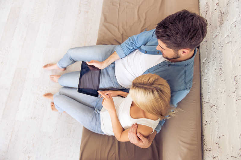 美丽年轻夫妇在家里坐着沙发一起看平板电脑