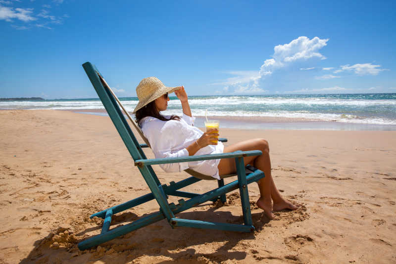 在海边戴着草帽喝果汁享受的女人