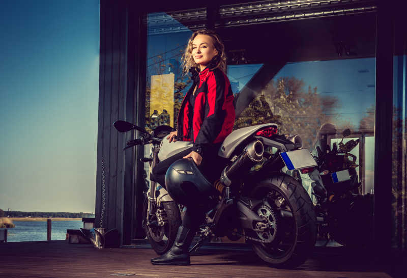 性感金发女郎穿着红色皮夹克在摩托车旁摆姿势