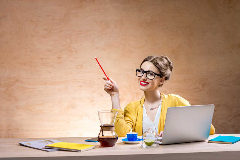 木桌上的咖啡笔记本电脑和坐在桌旁一个拿着铅笔的女人