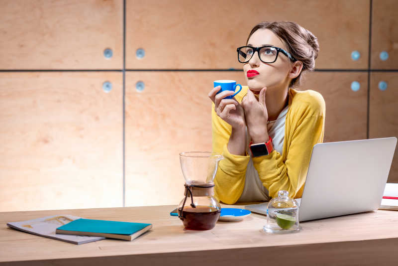 在木质桌板上喝着咖啡用着笔记本电脑的美丽女人