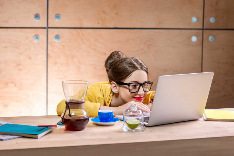 正在木桌上一边和咖啡一边使用笔记本电脑的美女