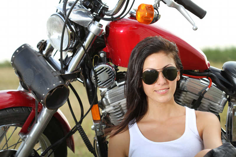 草地上站在摩托车旁边的年轻女子