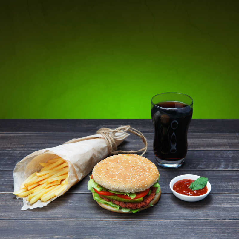 绿色背景下木桌上的汉堡薯条可乐