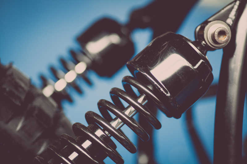 蓝色背景下摩托车悬架上的金属色减震器