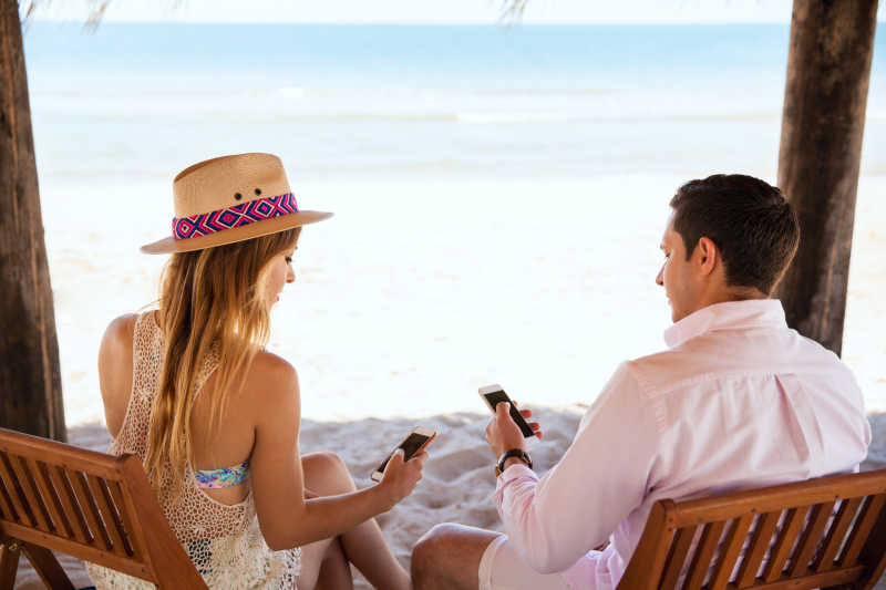 海滩度假的年轻夫妇正在玩手机