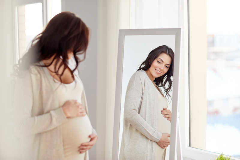 幸福的孕妇望着镜子