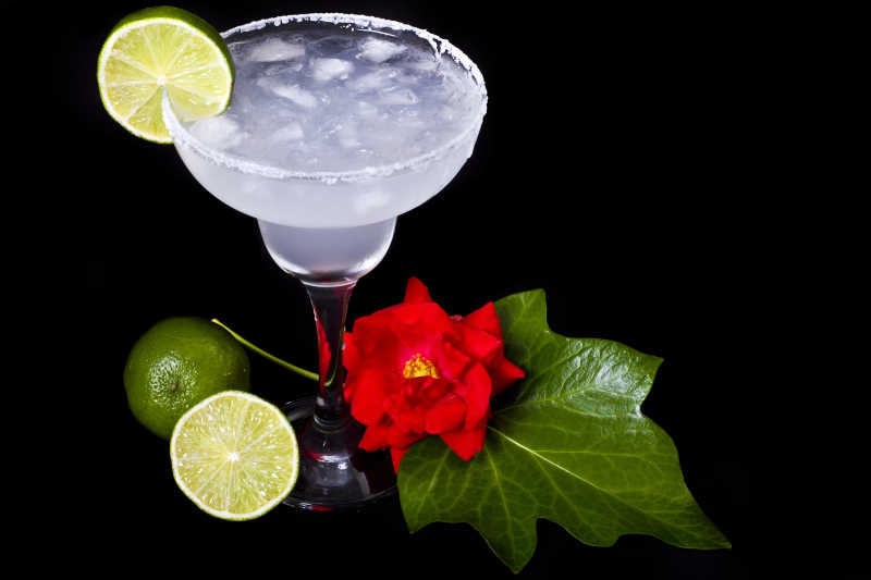 黑色背景下有花朵和柠檬装饰的桌上的鸡尾酒