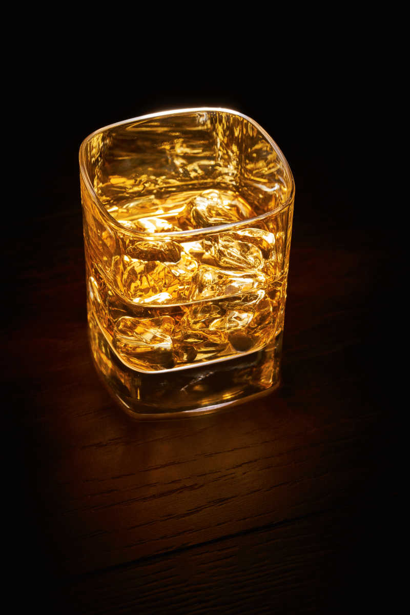 木桌上被光打亮的威士忌玻璃杯