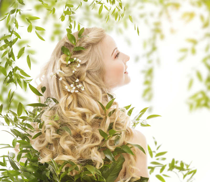 绿叶背景下的金色长卷发的年轻女孩