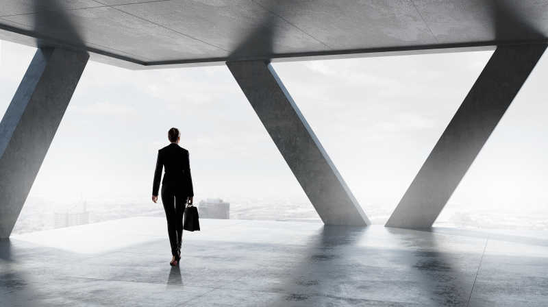 穿着西服的女性在落地窗前提着公文包