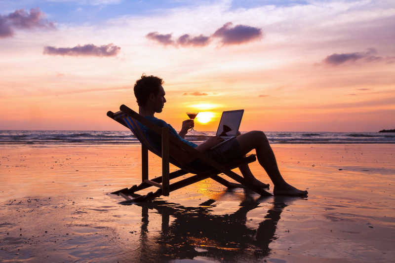 夕阳下男人坐在海滩休闲椅上办公