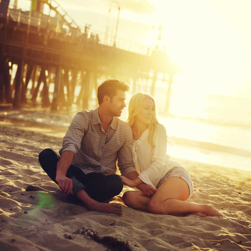 夕阳下金色的沙滩上坐着一对幸福的情侣