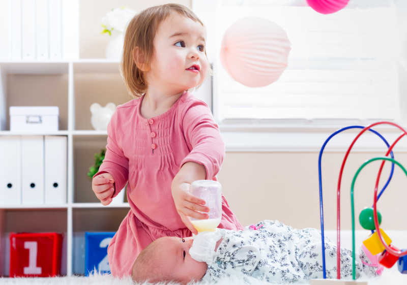 给新生婴儿妹妹喂奶的可爱小女孩