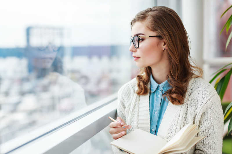 穿着白色的毛衣戴眼镜拿着笔记本和笔的年轻美女