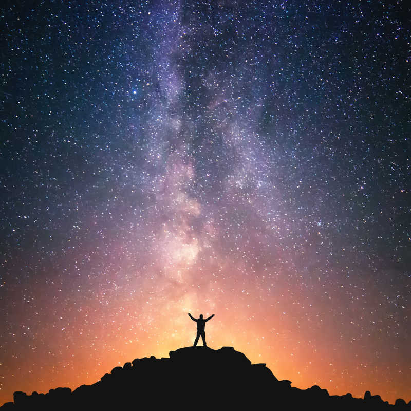 一个人站在银河旁边的山顶上双手举向空中