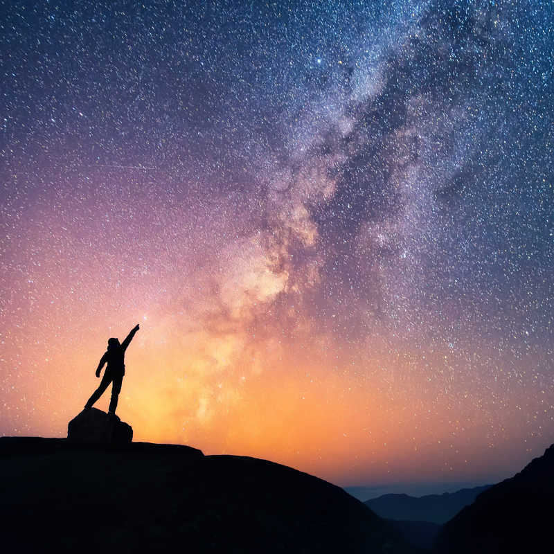 一个人站在银河系旁边指着一颗明亮的星星