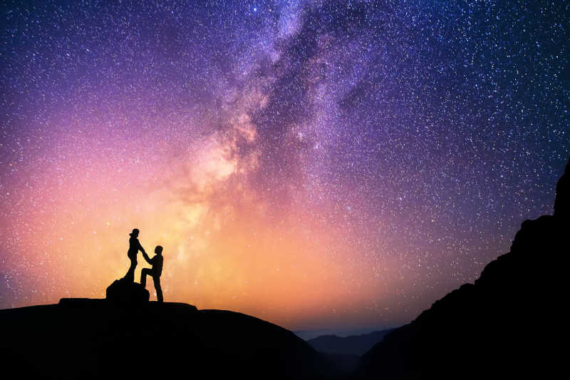 在美丽的银河系背景下浪漫的情侣手拉手在山上