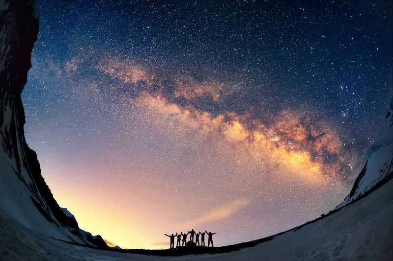 一群人手拉手对着山中的银河站在一起