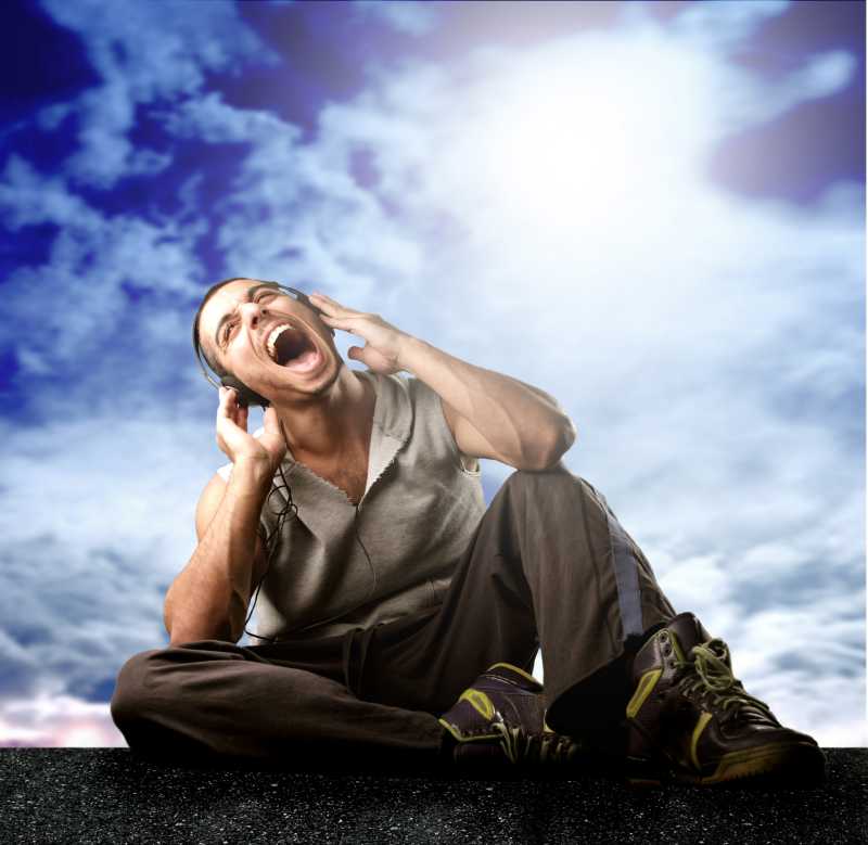 天空下坐在地上听音乐唱歌的男人