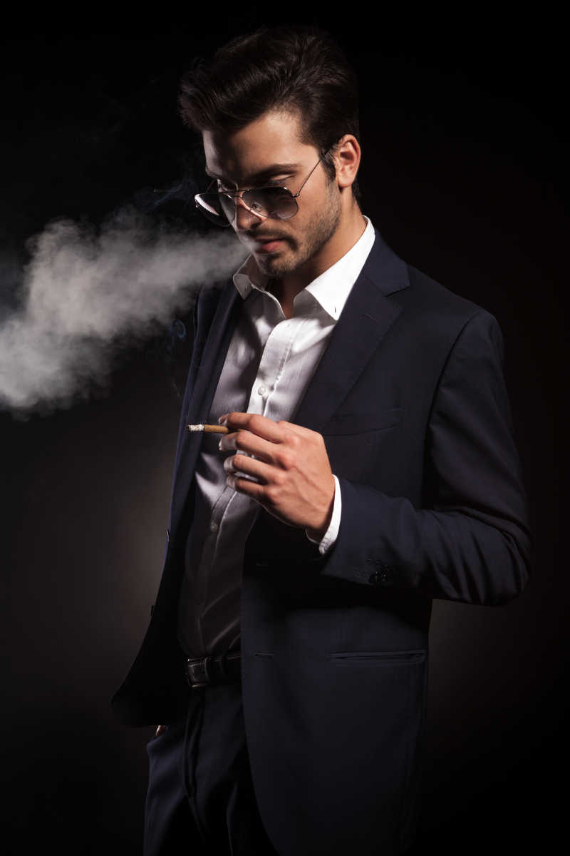 年轻英俊的商人一边手里拿着一支烟一边吹着烟