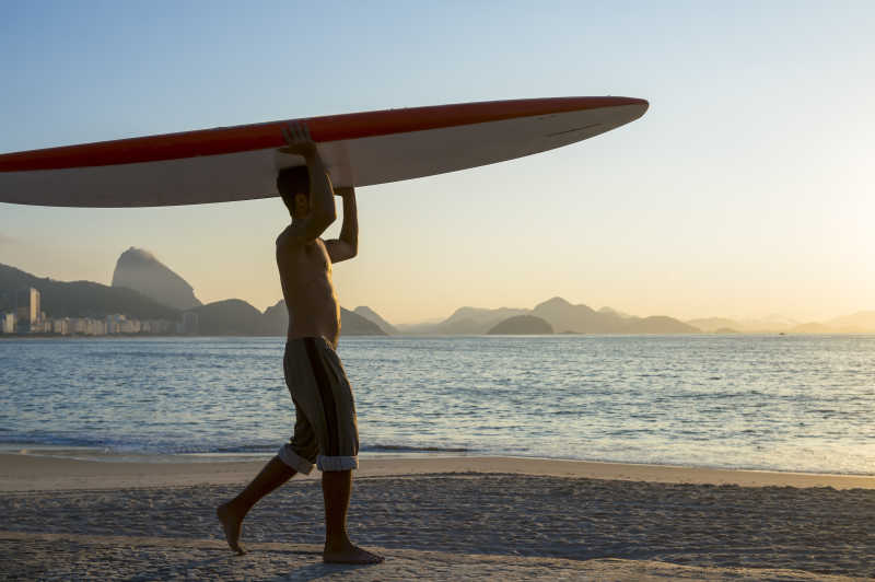 黄昏的海滩上一个举着冲浪板的男人