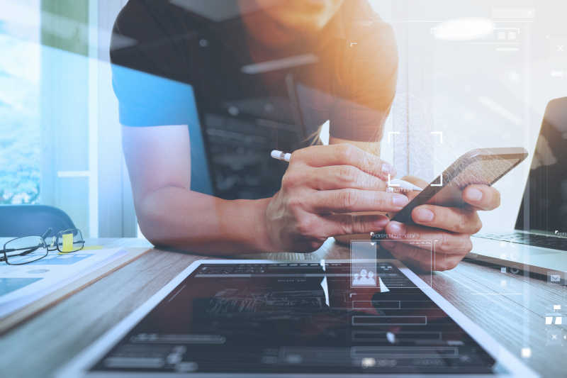 趴在木桌上使用笔记本电脑和手机工作的网站设计师