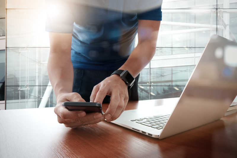 弯腰在木桌前商人使用笔记本电脑和手机的商人