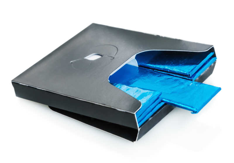 白色背景下黑色纸盒里盛放的蓝色铝箔包装的口香糖糖