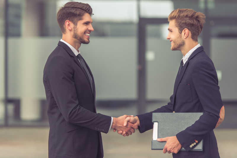 两个身着古典西装的英俊青年商人正在握手