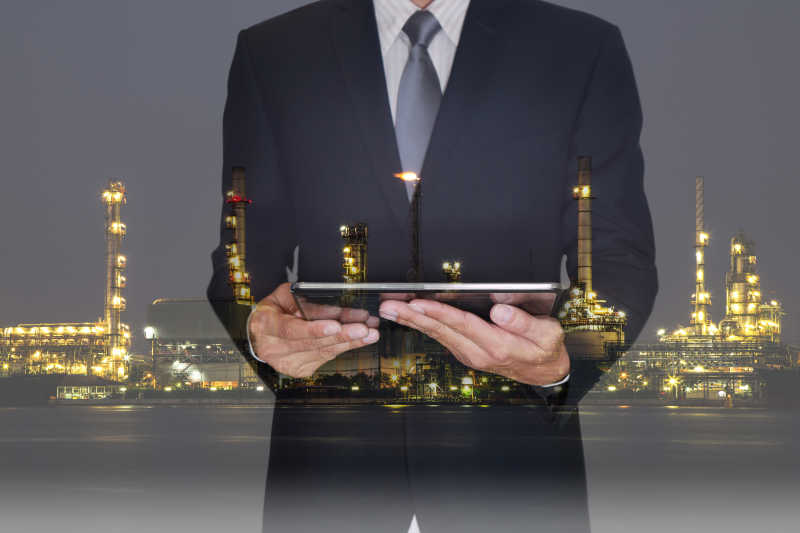 手持平板的商人和夜间的炼油工厂双重曝光