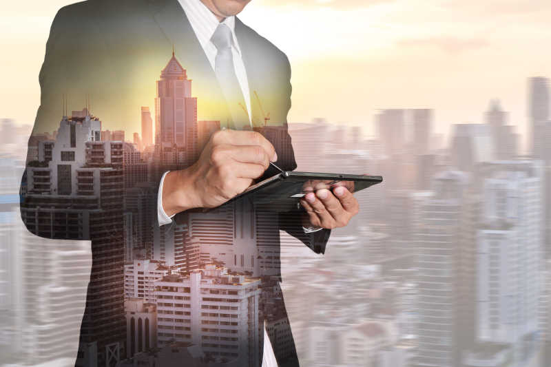 操纵平板电脑的商人和城市的日落双重曝光