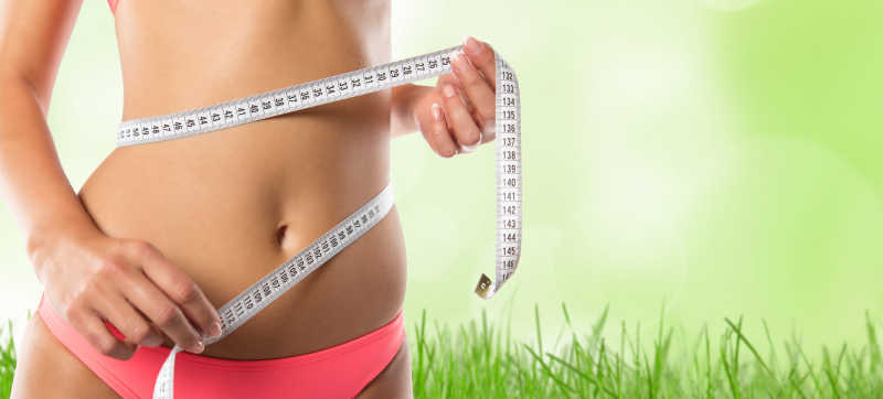 绿草背景上苗条的女人测量腰围