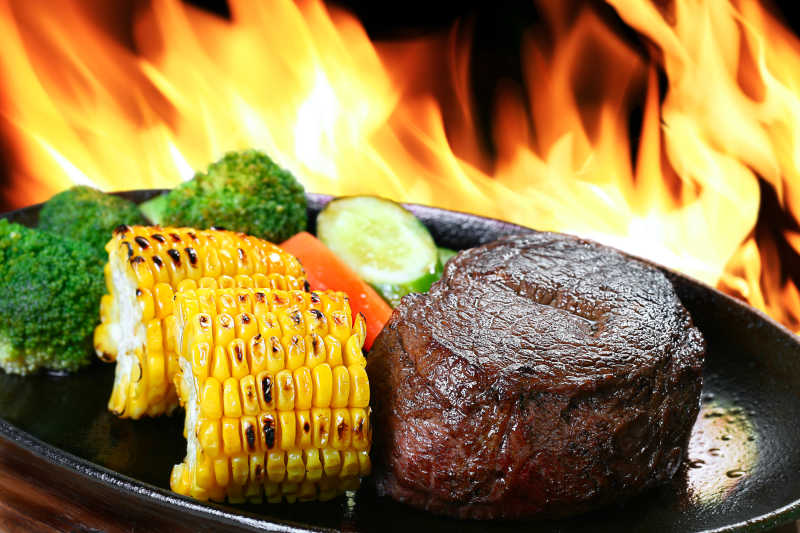 火焰背景中的烤牛排和蔬菜