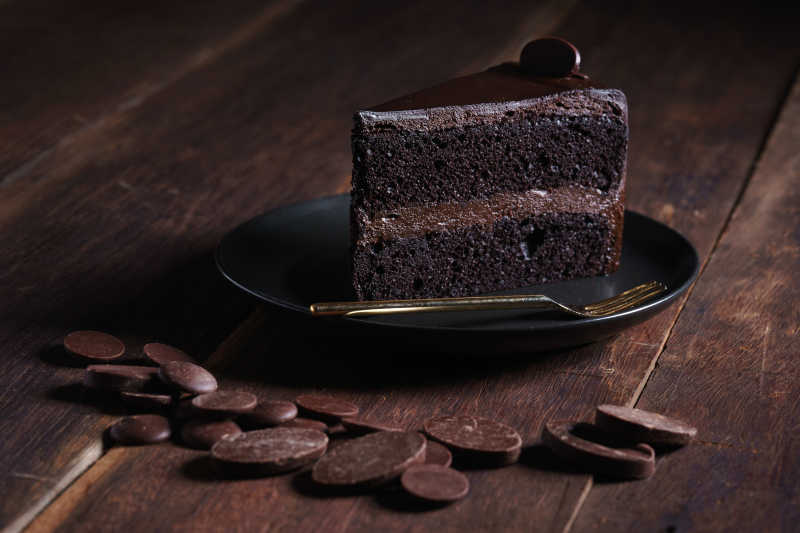 木桌上黑盘子里的美味巧克力蛋糕