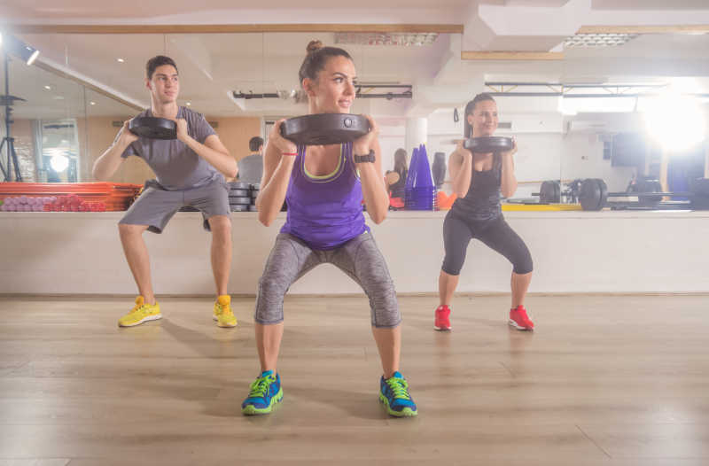 健身房里正在练习深蹲的学员