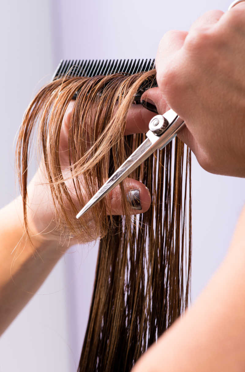 美发师用梳子和专业剪刀剪裁女客户的棕色长发