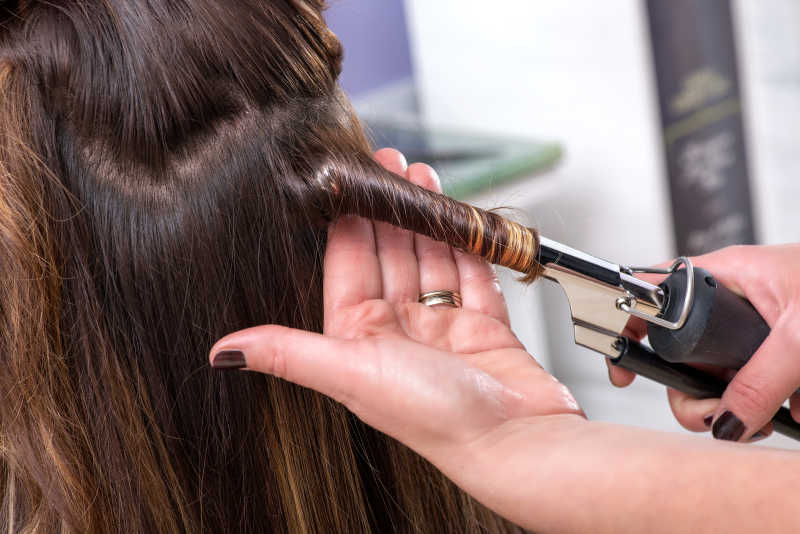 理发师在女顾客的长棕色头发上使用卷发器