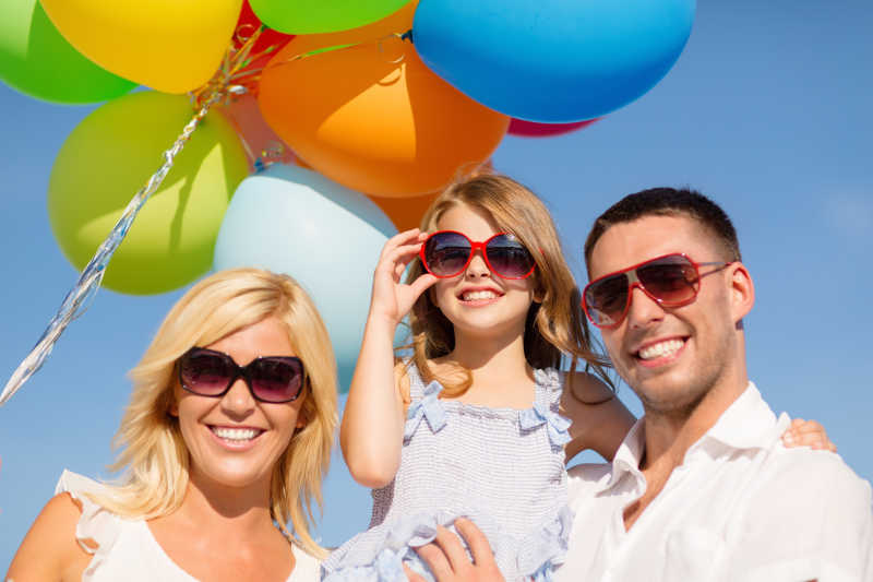 快乐的小女孩和父母一起手拿彩色气球合影