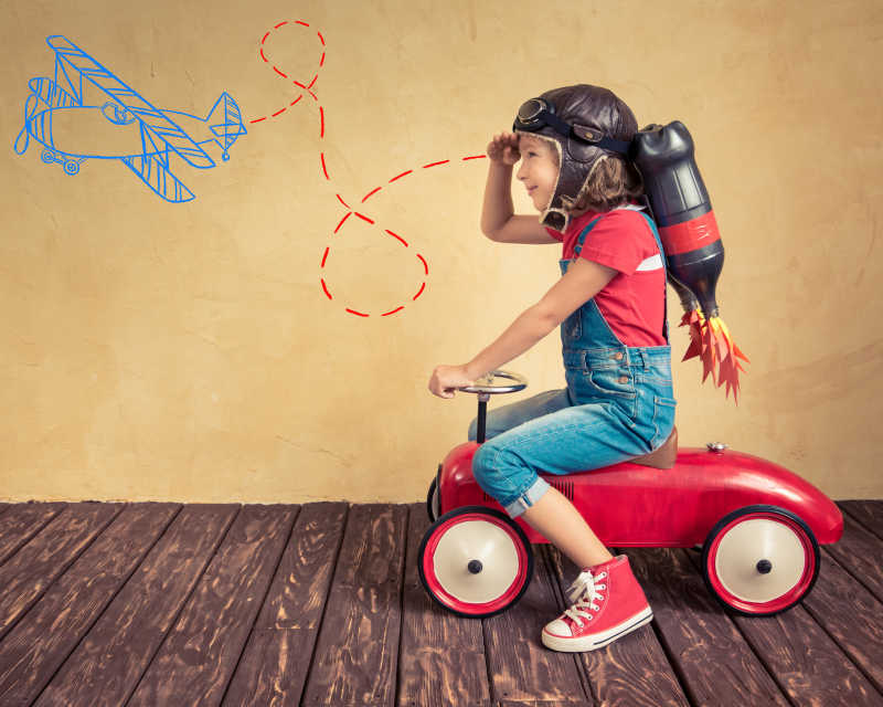 在木地板上背着喷气背包骑着玩具车的小孩子