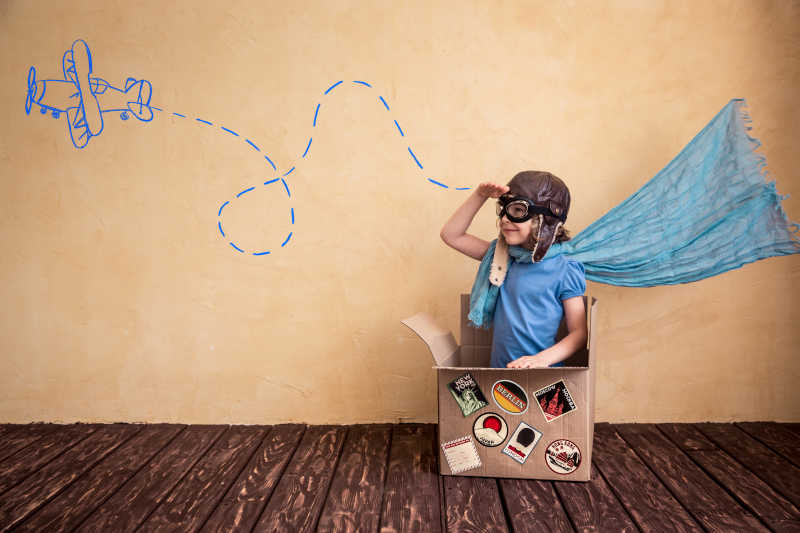坐在木地板的纸箱中穿着超人的衣服玩的孩子