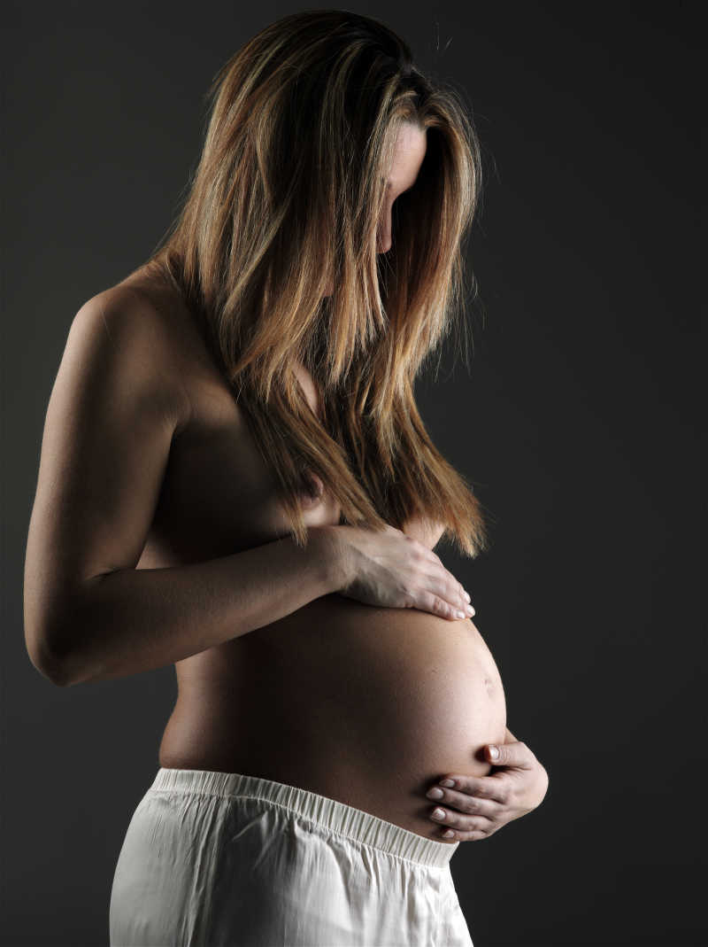 黑色背景下抚摸着肚子的孕妇