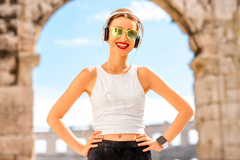 建筑拱门前戴着墨镜听音乐的快乐美女