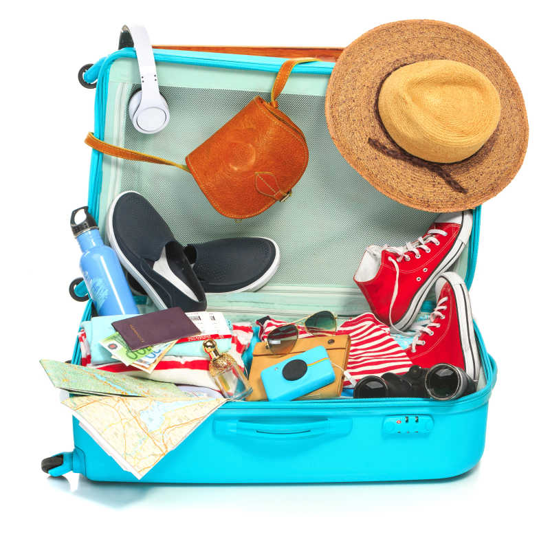 白色背景下放着鞋照相机和帽子的蓝色旅行箱
