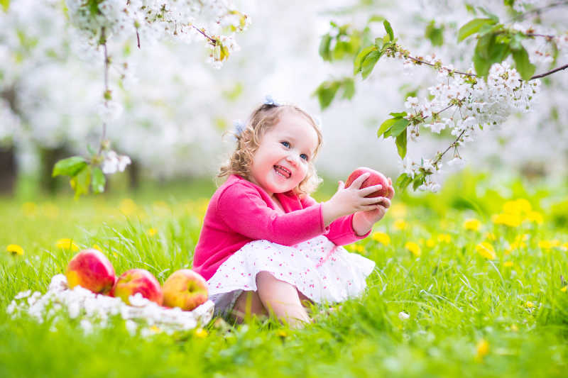 草丛上可爱的吃苹果的小女孩