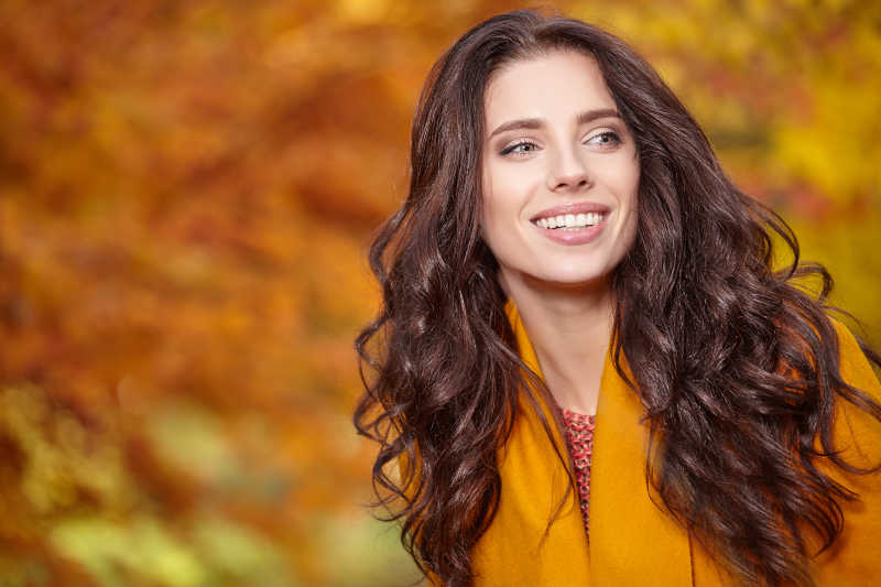 丽年轻女子在秋季的花园里微笑